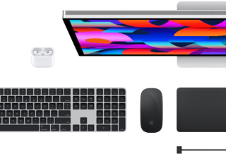 Mac-tilbehør vist ovenfra: Studio Display, AirPods, Magic Keyboard, Magic Mouse og Magic Trackpad