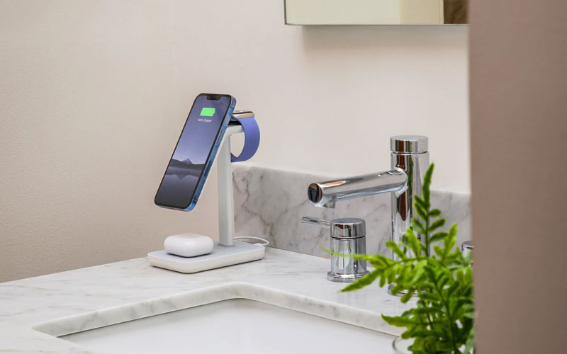 Apple iPhone, headphones and watch on a wireless stand on a sink in a bathroom