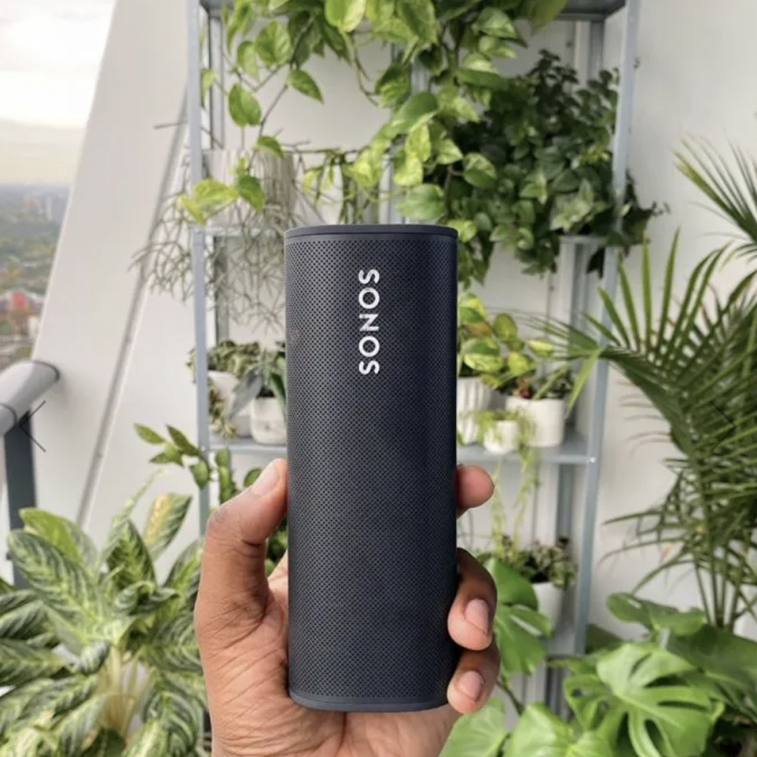 Sonos Roam speaker held in front of green plants